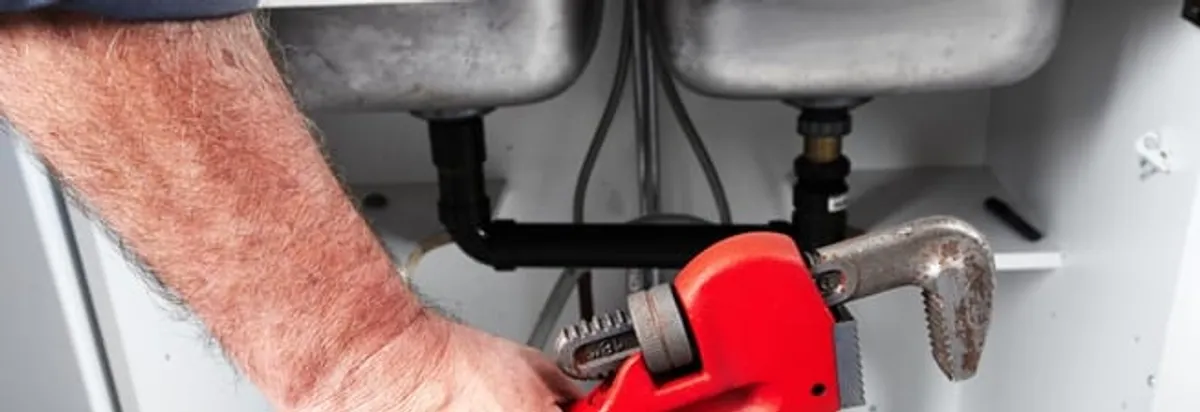 Garbage disposal repair technician tightening drain connections under a kitchen sink in Albany, NY