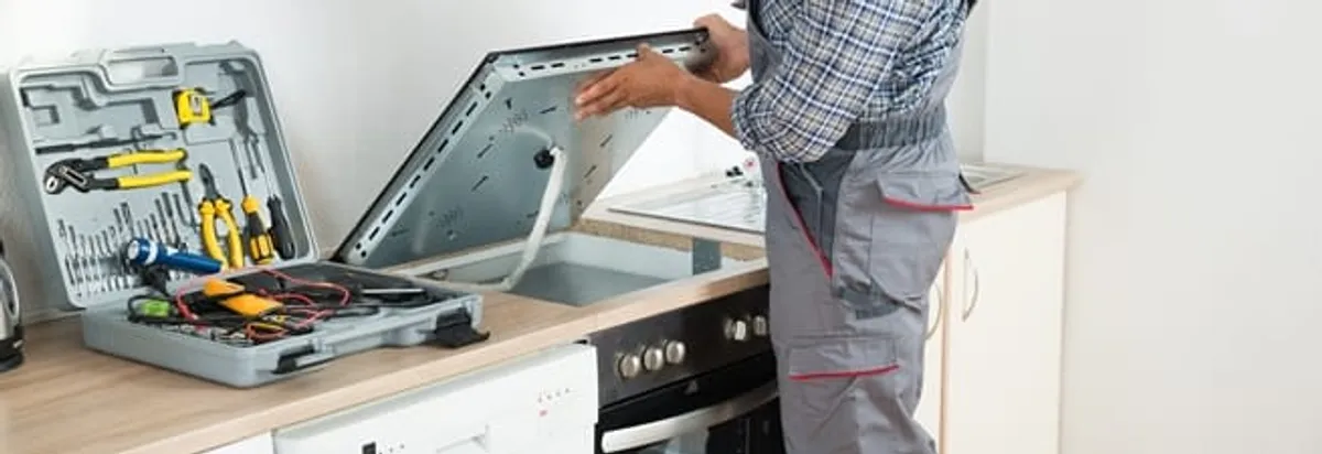 Cooktop repair technician lifting a built-in stovetop for service in Albany, NY